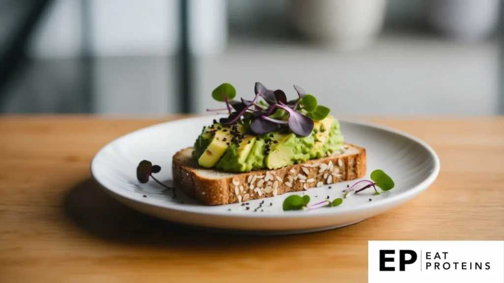 A slice of whole grain toast topped with mashed avocado and sprinkled with fresh microgreens on a white ceramic plate