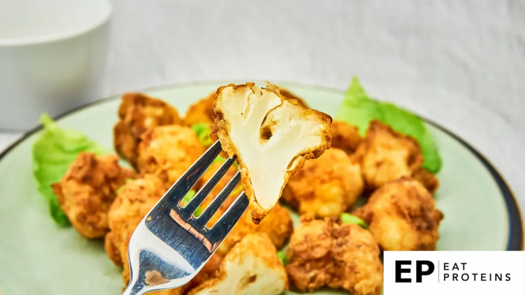 A platter of crispy buffalo cauliflower bites surrounded by fresh celery and carrot sticks, with a side of creamy ranch dressing for dipping