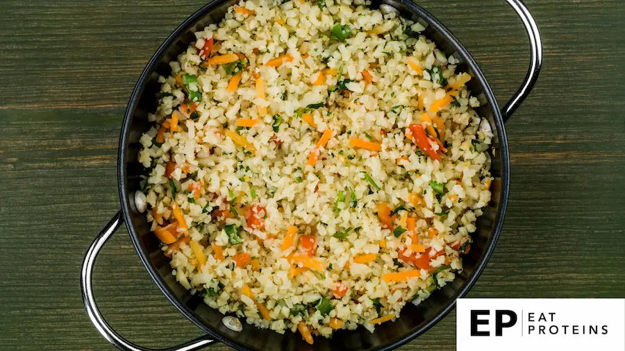 A sizzling skillet of cauliflower fried rice on wooden table