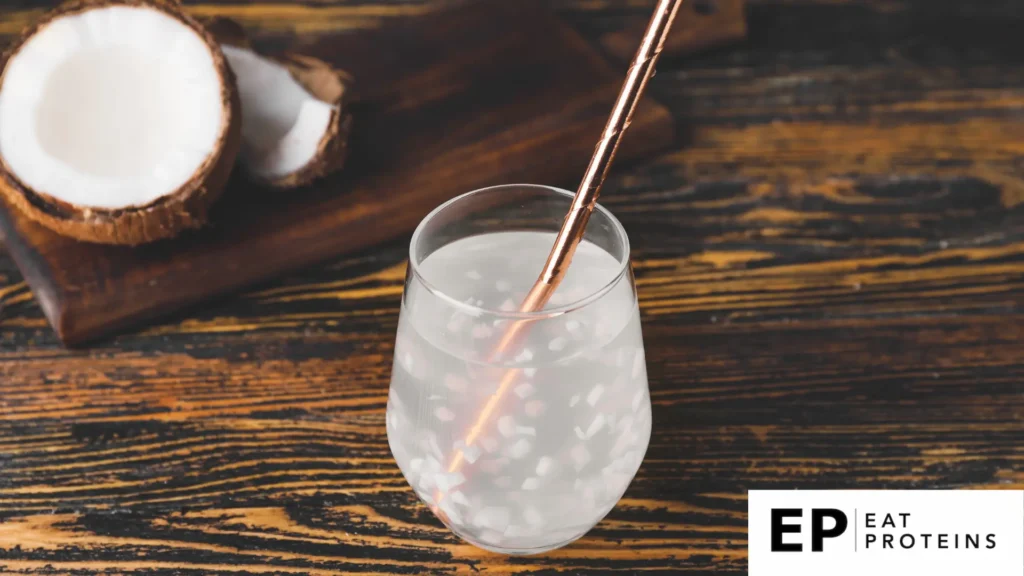 A glass of coconut water surrounded by fresh coconuts