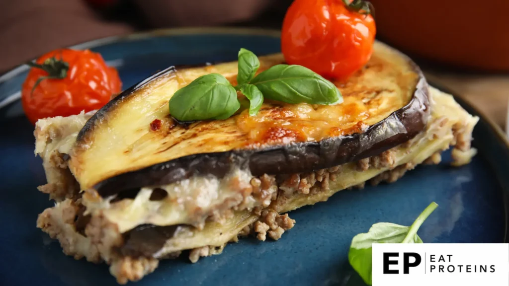 A colorful array of fresh eggplants, tomatoes, and herbs arranged on a wooden cutting board next to a stack of gluten-free lasagna noodles and a bowl of dairy-free cheese