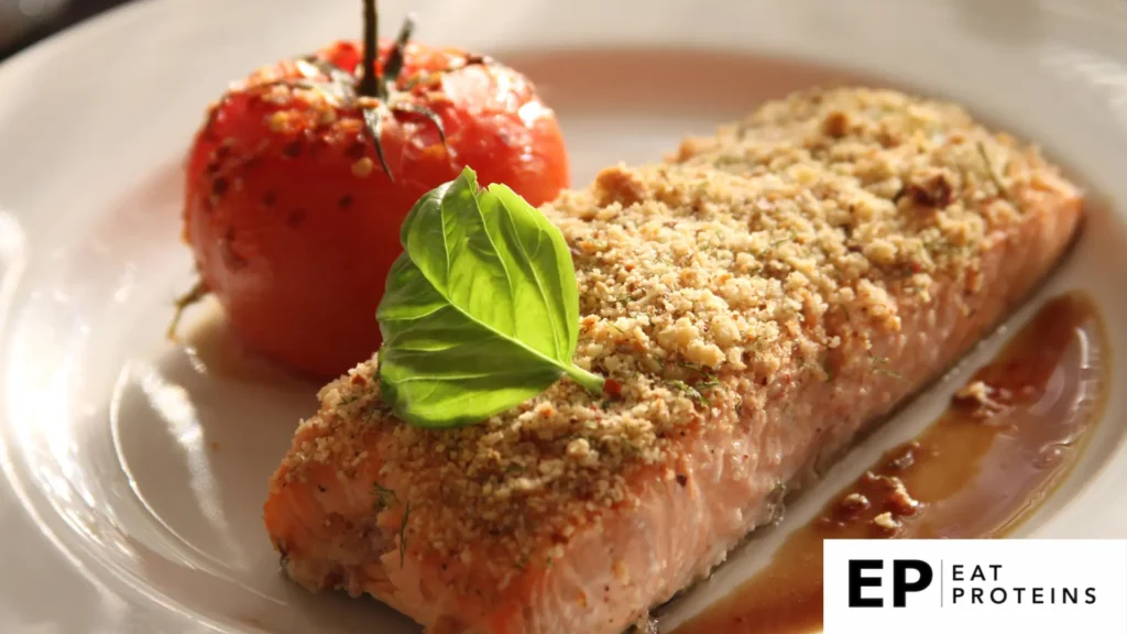 A plate of garlic parmesan salmon surrounded by colorful cooked tomato, and fresh herbs