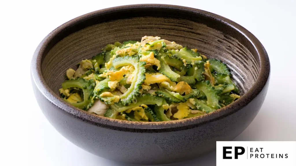 The image shows a bowl filled with a traditional Okinawan dish called "Goya Champuru." The dish consists of stir-fried bitter melon (goya), eggs, and tofu or other proteins, commonly pork