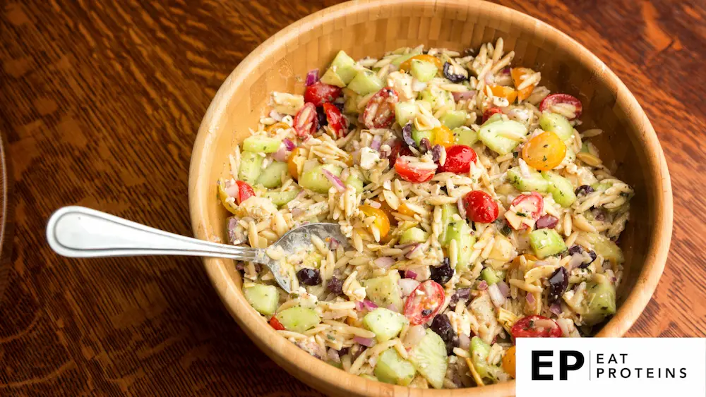 This image showcases a Mediterranean Orzo Pasta Salad, a hearty and colorful dish perfect for a Mediterranean diet. The salad contains cooked orzo pasta mixed with diced cucumbers, cherry tomatoes (both red and yellow), red onion, Kalamata olives, and crumbled feta cheese. The salad appears to be dressed in a light vinaigrette, which likely includes olive oil, lemon juice, herbs, and seasoning.