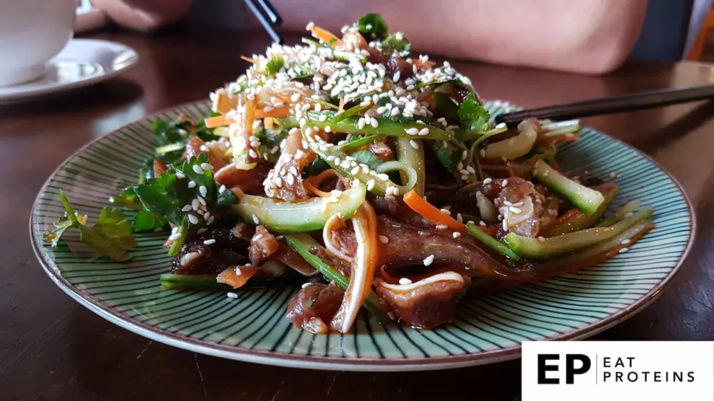 The image shows a plate of "Mimiga," an Okinawan dish made from thinly sliced pig's ear mixed with vegetables like cucumber and carrot. The dish is topped with sesame seeds and garnished with fresh cilantro