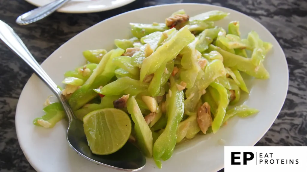 The image shows a plate of "Nabera Irichi," a stir-fried Okinawan dish made with angled luffa (sponge gourd) and small pieces of meat. The light green gourd slices are cooked to a tender consistency and are served with a wedge of lime