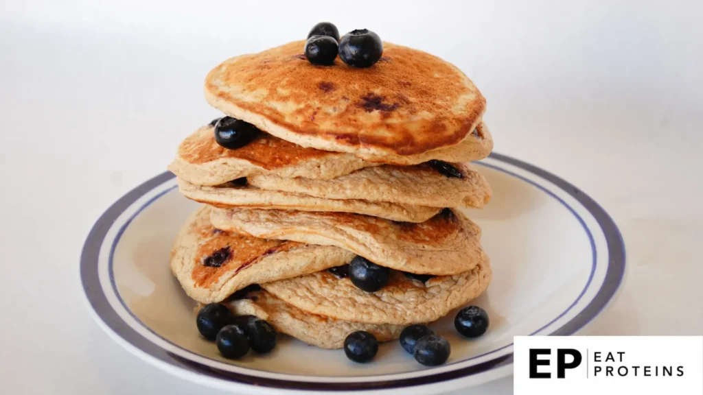 A stack of oat bran pancakes surrounded by fresh fruit and a dollop of yogurt on a white plate