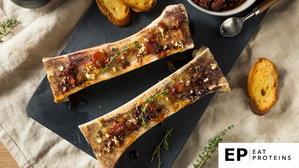 A rustic wooden table set with a platter of roasted bone marrow, surrounded by fresh herbs and crusty bread