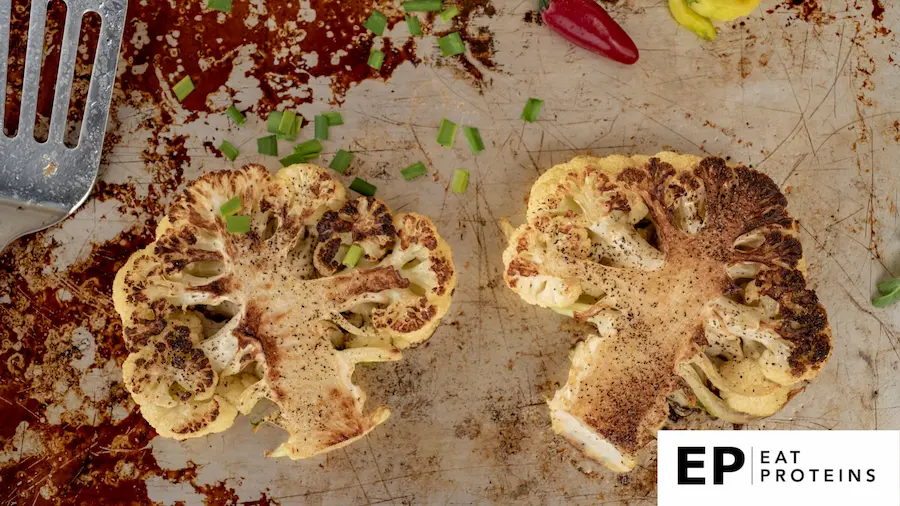 A platter of golden brown cauliflower steaks surrounded by vibrant, fresh ingredients