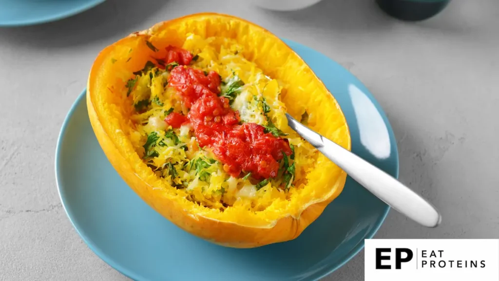 The image shows a spaghetti squash half served as a dish on a blue plate. The squash is roasted, with its stringy flesh resembling spaghetti, topped with herbs, and garnished with a tomato-based sauce, likely resembling a spaghetti-style primavera. The vibrant yellow of the squash contrasts with the red sauce and green herbs, making the dish visually appealing.