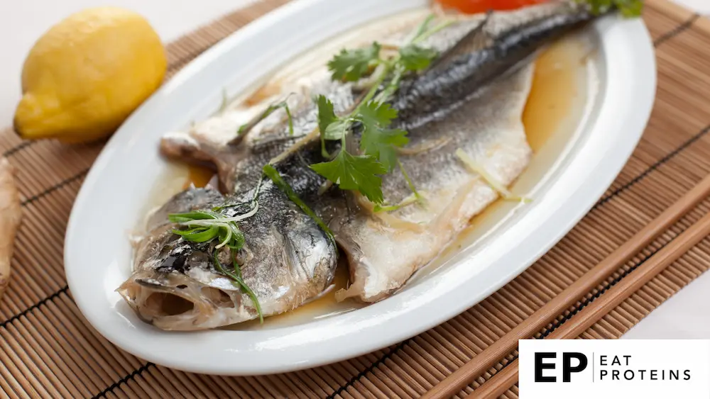 A plate of steamed white fish surrounded by colorful vegetables and herbs