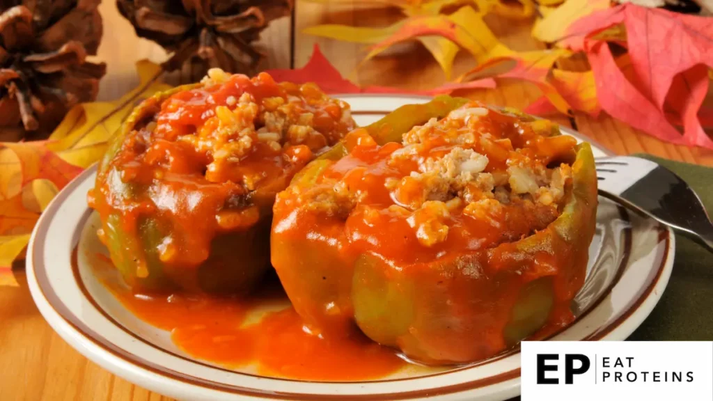 The image shows two stuffed green bell peppers on a plate, filled with a mixture of ground meat, rice, and a savory tomato-based sauce. The stuffing is generously covered with a rich, chunky tomato sauce, adding a vibrant red color that contrasts with the green bell peppers