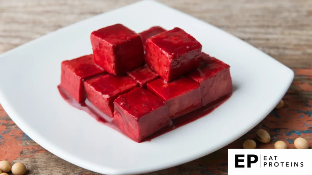 The image shows a plate of "Tofuyo," a traditional Okinawan delicacy made from fermented tofu. The tofu cubes are deep red, coated in a rich sauce, and neatly stacked on a white plate. The dish has a smooth and glossy texture, indicating its fermentation process