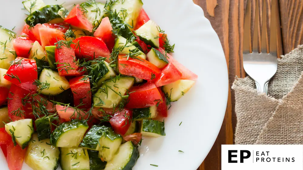 A bowl of tomato and cucumber salad drizzled with olive oil on a rustic wooden table