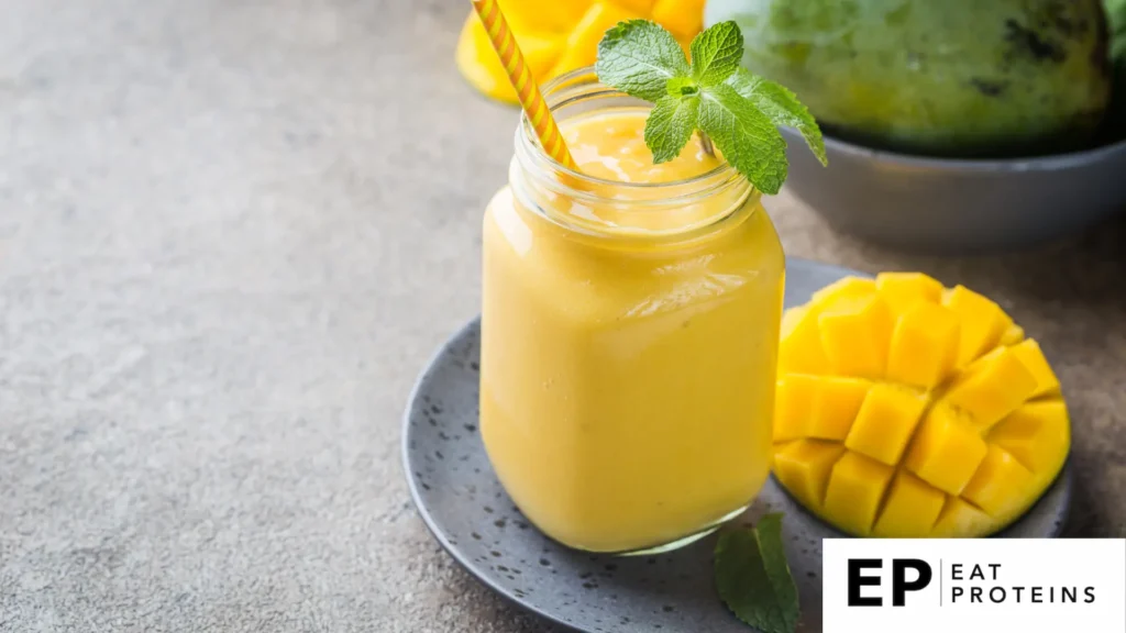 A glass of mango juice and a straw surrounded with half mango