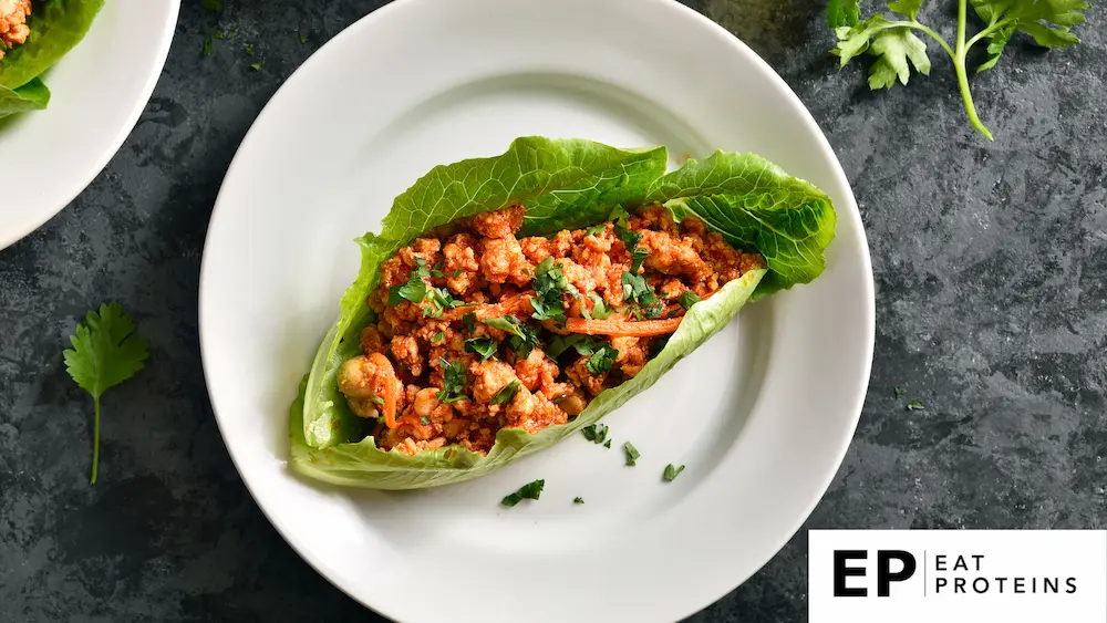 Fresh lettuce leaves filled with turkey and colorful vegetables on a clean, white plate