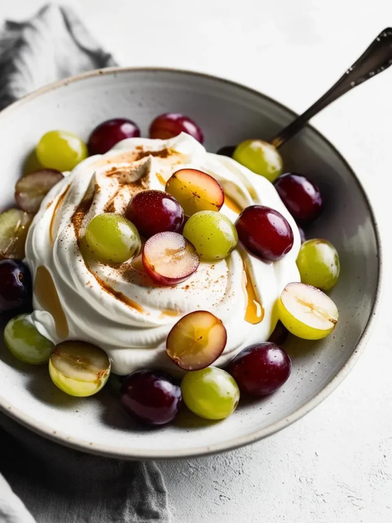 A bowl of creamy Greek yogurt topped with fresh red and green grapes, drizzled with honey, and sprinkled with cinnamon. The dish looks light, refreshing, and perfect for a healthy breakfast or snack.