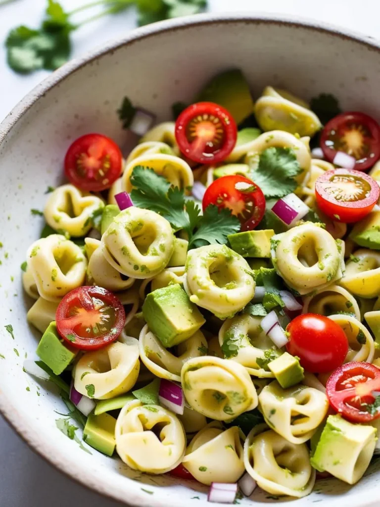 A vibrant and refreshing pasta salad with tortellini, avocado, cherry tomatoes, red onion, and a creamy pesto dressing. The salad looks light and perfect for a summer meal.