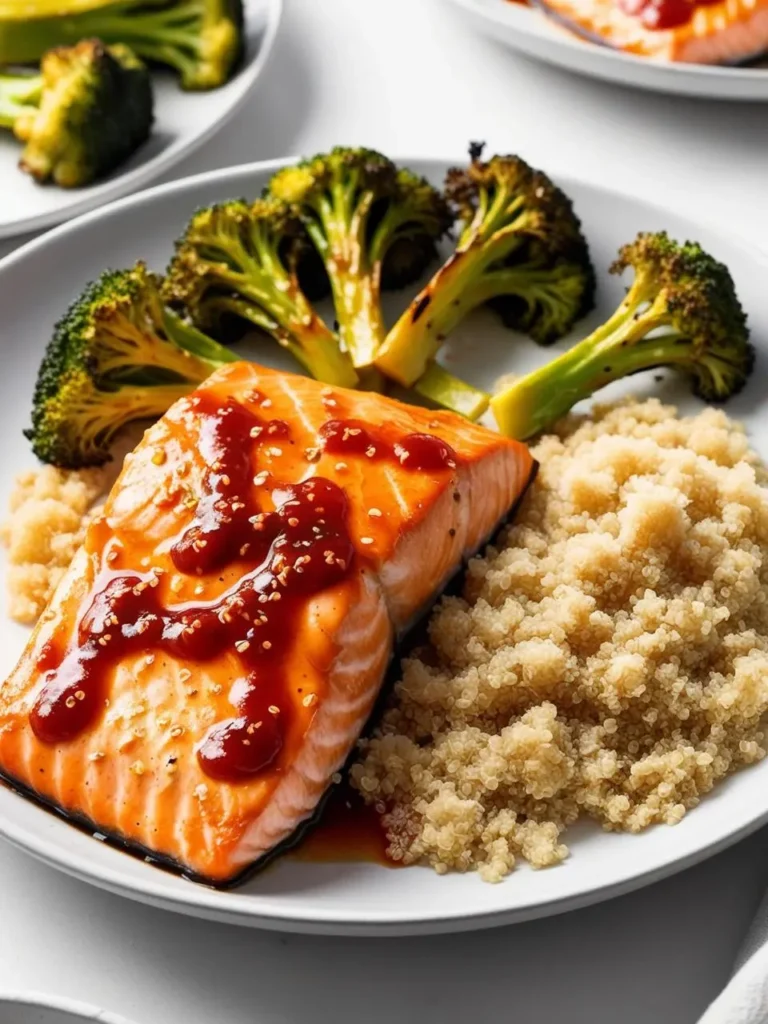 A plate of pan-seared salmon glazed with a sweet chili sauce. The salmon is served on a bed of fluffy quinoa and accompanied by a side of roasted broccoli. The dish looks delicious and healthy.