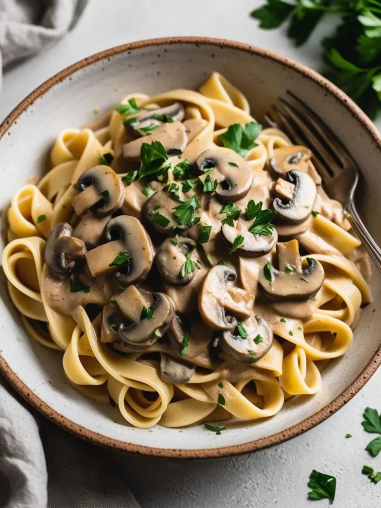 A bowl of creamy mushroom pasta with fettuccine noodles, topped with fresh parsley. The pasta is coated in a rich, mushroom sauce, making it a comforting and satisfying meal.